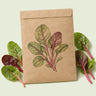 Kraft seed packet illustrated with Apple Blossom Swiss Chard Baby Greens, with fresh Apple Blossom Swiss Chard Baby Greens beside it