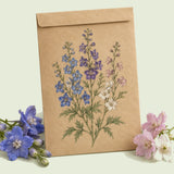 Kraft seed packet illustrated with Butterfly Blend Delphinium, with fresh Butterfly Blend Delphinium beside it