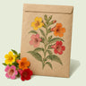 Kraft seed packet illustrated with Magic Mix Monkey Flower, with fresh Magic Mix Monkey Flower beside it