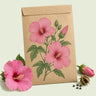Kraft seed packet illustrated with Pink Rose Mallow, with fresh Pink Rose Mallow beside it
