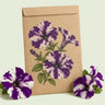 Kraft seed packet illustrated with Purple Tie Dye Petunia, with fresh Purple Tie Dye Petunia beside it