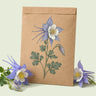 Kraft seed packet illustrated with Rocky Mountain Blue Columbine, with fresh Rocky Mountain Blue Columbine beside it