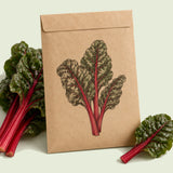 Kraft seed packet illustrated with Ruby Red Swiss Chard, with fresh Ruby Red Swiss Chard beside it