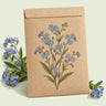 Kraft seed packet illustrated with Victoria Blue Forget Me Not, with fresh Victoria Blue Forget Me Not beside it
